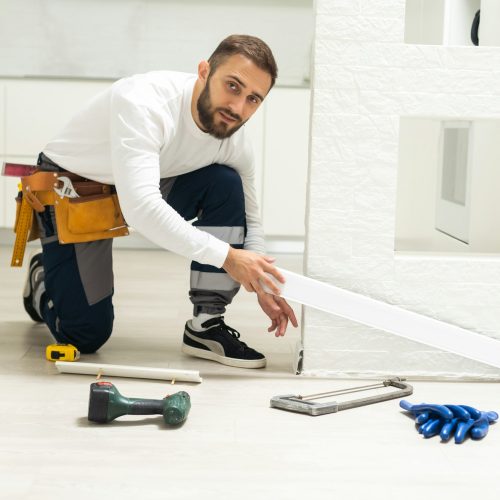 A man installs a floor skirting board. Fixing the plastic skirting board with screws to the wall
