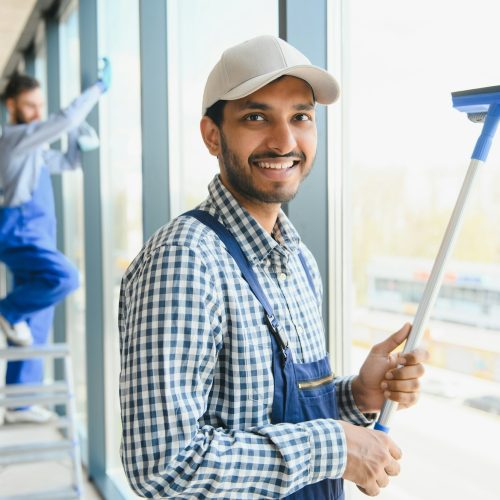 Male janitor cleaning window in office