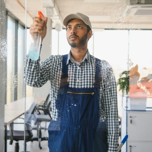 Male janitor cleaning window in office