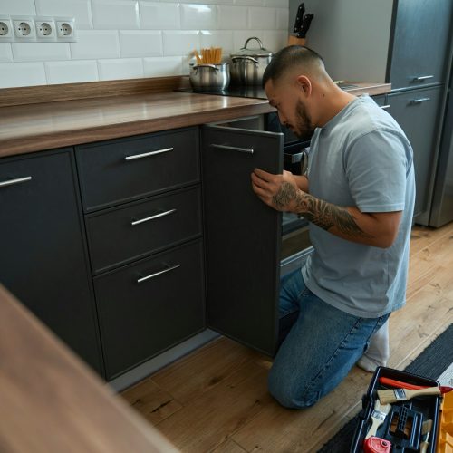 Man crouched at door of kitchen cabinet for minor repairs