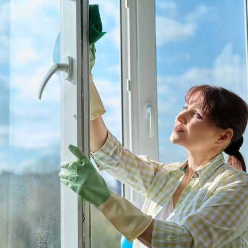 Woman cleaning windows at home using spray and microfiber cloth